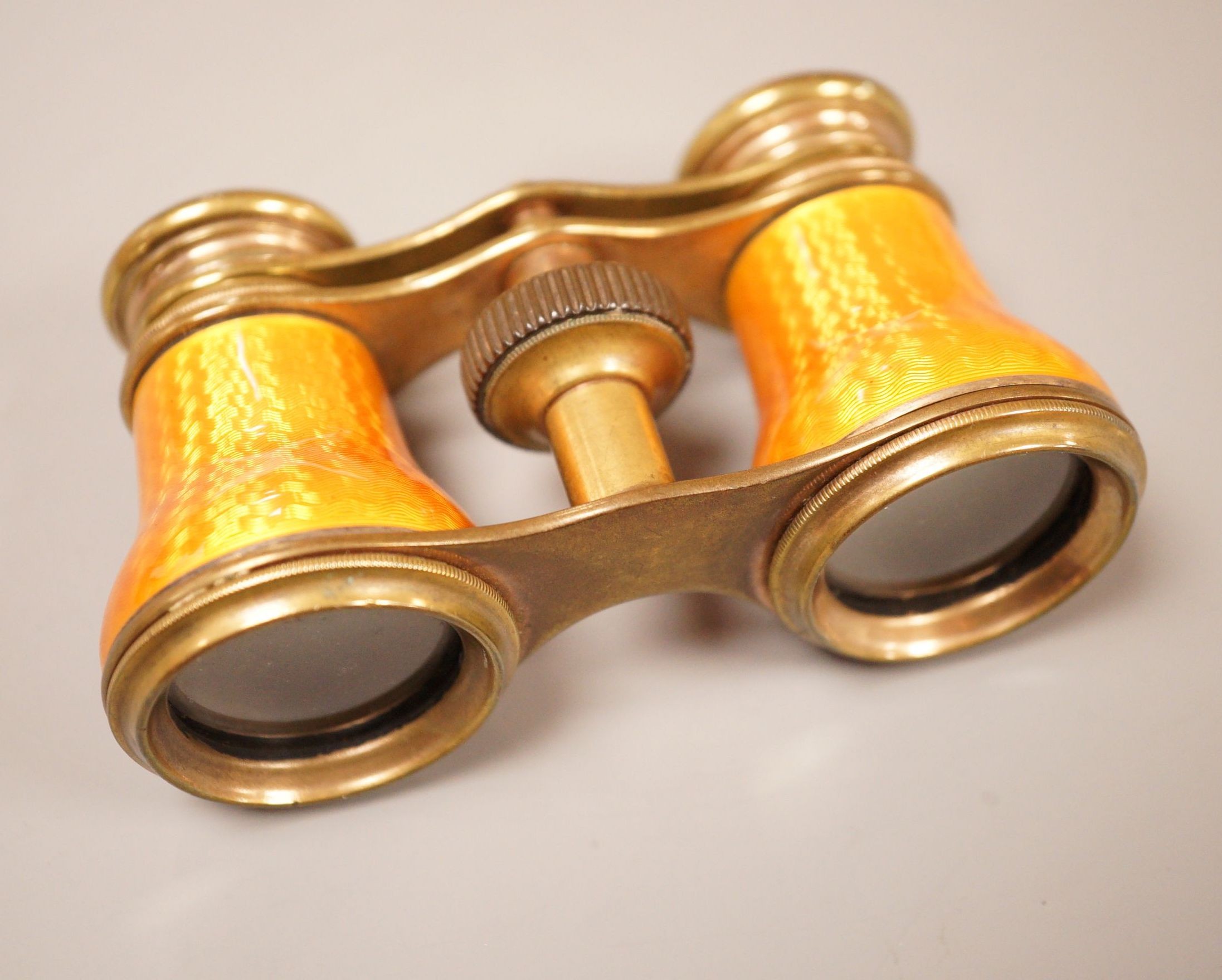 A pair of German orange enamelled opera glasses, inscribed Fabr Emil Busch, Rathenow to the left lens, and E. Petitpierre, BerlinFriedrichstr. to the right lens, 10cm wide
